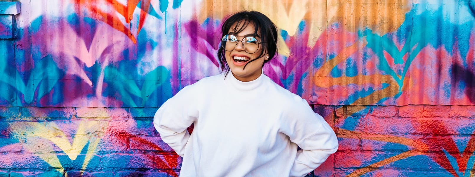 A smiling Position Digital team member in front of a vibrant, colourful mural.