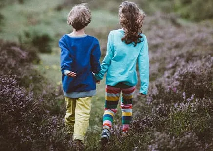 Two children walking hand in hand through a field, symbolising authentic partnership.