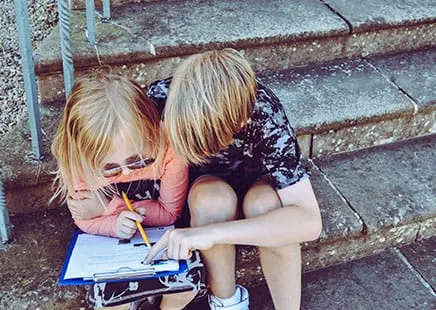 Two children collaborating on a clipboard, symbolising teamwork and shortlisting.