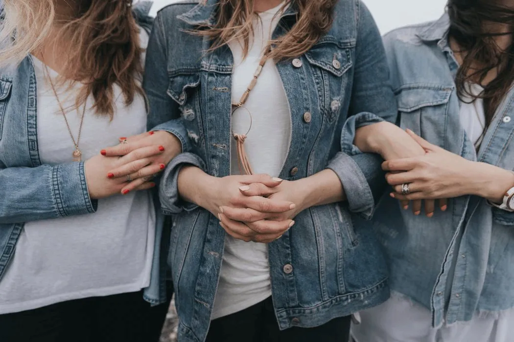 Three people in denim jackets link arms, symbolising collaboration and partnership.