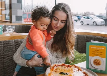 A woman and child enjoy a meal at a restaurant. The child points at a pizza.