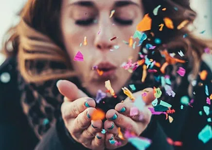 A woman blows colorful confetti, symbolizing the vibrant impact of a B2B SaaS SEO agency and AI SEO company for startups.