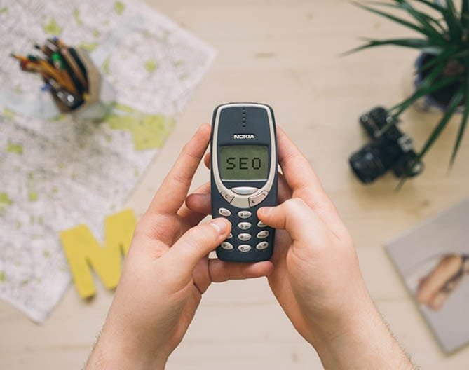 Hands hold a phone displaying 'SEO', symbolising organic search strategy work.