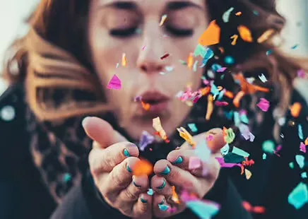 A woman blows colorful confetti, symbolizing celebration.
