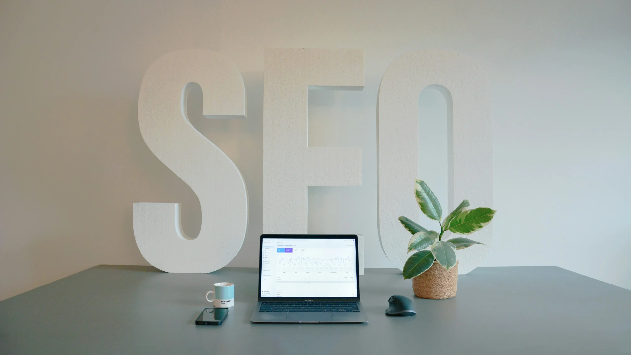 A laptop showing an SEO tool on the screen and a giant "SEO" word on the wall.